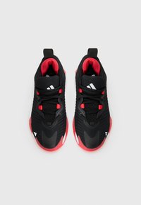 Chaussures de sport noires avec des accents rouges, tige en maille et semelle en caoutchouc. Comprend un col rembourré et un logo blanc sur le côté latéral.