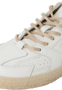 Baskets en cuir blanc avec lacets beige et semelle beige texturée, montrant des coutures détaillées et un design superposé sur la tige.