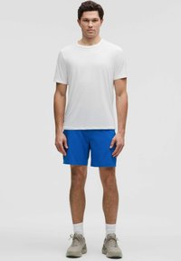 Weißes kurzärmliges T-Shirt und blaue Shorts. Die Shorts sind leicht und haben eine glatte Textur. Kombiniert mit beigen Sneakers und weißen Socken.