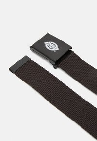 Svart webbingbälte med en matte svart metallspänne. Har "Dickies"-logotypen på spännet, textil med struktur och rena kanter.