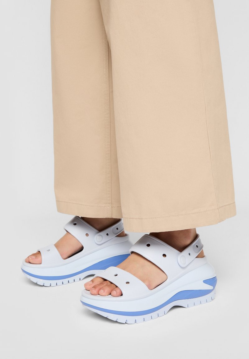 Hvite plattform sandaler med blå accenter, med tykk såle, justerbare stropper og åpen tå-design, brukt med beige vide bukser.