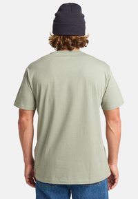 Lys grøn bomulds t-shirt med en afslappet pasform, korte ærmer og rund halsudskæring, parret med mørke denim jeans og en marineblå hue.