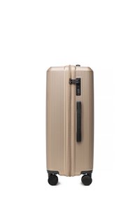 Hard-shell beige koffer met verticale ribbels, zwarte zijhandgreep, vier wielen en een ingebouwd cijferslot.