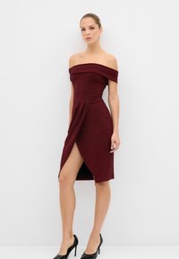 Burgundi off-the-shoulder mekko, jossa on kapea muotoilu, kietaisfrontti ja sivuhalkio. Valmistettu teksturoidusta kankaasta ja yhdistetty mustiin korkokenkiin.