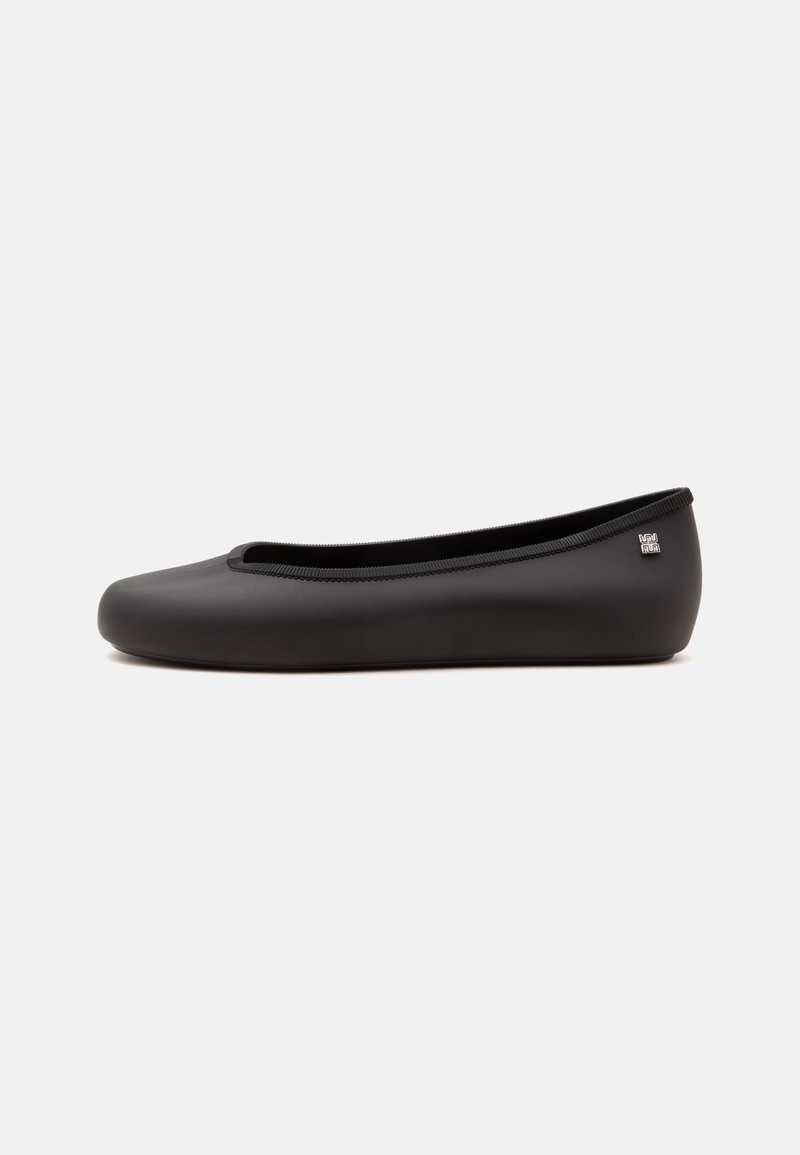 Chaussure ballerine plate noire avec bout rond et petit logo argenté sur le côté du talon, présentée sur fond blanc uni.