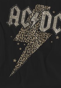 Schwarzes T-Shirt mit großem, abgenutztem grauem "AC/DC"-Text, einem goldenen Leopardenmuster-Blitz und kleinen goldenen Sternen.