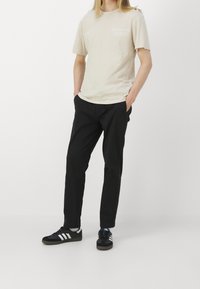 Beżowa bawełniana koszulka z graficznym napisem, zestawiona z czarnymi spodniami. Obuwie w kolorze czarnym i białym ma paski na casualowym wzorze sneakersów.