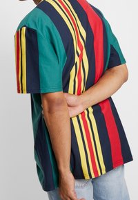 Kortärmad t-shirt med vertikala ränder i grön, marinblå, röd och gul. Tillverkad av bomull med en avslappnad passform och rundad hals.