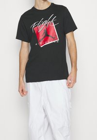 Černé bavlněné tričko s výraznou červenou a bílou grafikou s nápisy "Flight" a "Air Jordan", klasický kulatý výstřih, krátké rukávy.