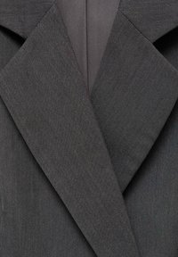 Šedý oblekový sako s klopovým límcem, texturovanou tkaninou a strukturovanými klopami. Mezi detaily jsou vertikální pruhy a hladká podšívka.