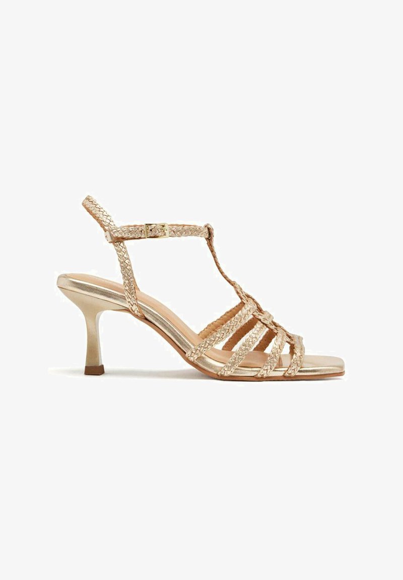 Sandalia de tacón alto con tiras en metalizada dorada, con tiras trenzadas, diseño de barra en T, hebilla ajustable en el tobillo y un tacón delgado.