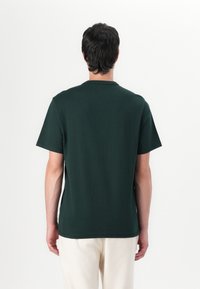 Camiseta de algodón verde oscuro con mangas cortas y cuello redondo, mostrada desde la parte posterior, con una textura suave y ajuste relajado.