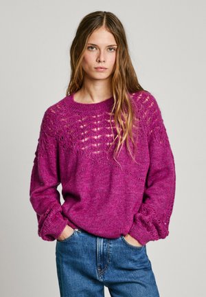Fuchsia knit sweater with a loose fit, featuring a textured yoke, intricate lace details, and ribbed cuffs, paired with denim jeans.