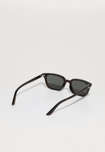 Lunettes de soleil en écaille de tortue avec des verres foncés, monture carrée et matériau en plastique lisse. Présente un logo discret sur la branche.