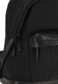 Rucsac negru din nylon cu accente din piele netedă. Are un buzunar cu fermoar și o formă structurată cu detalii cusute.