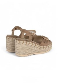 Beige Keilsandaletten mit einer strukturierten Espadrille-Sohle. Sie haben einen Vorderriemen mit einer dekorativen Schnalle und einem verstellbaren Knöchelriemen. Das Material ist weich.
