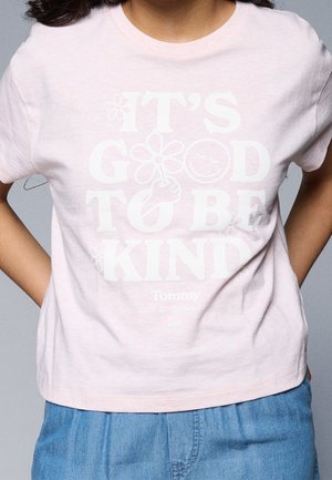 Kvinde iført lyserød T-shirt med hvid tekst "Det er godt at være venlig" med blomster, et smilende ansigt og tommelfinger op-illustration.
