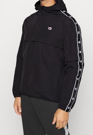 Black lightweight jacket with a front pocket, half zip, and hood. Features white logo accents along the sleeves and a smooth texture.