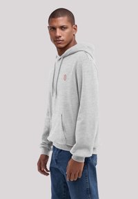 Hellgrauer Hoodie mit einer Vordertasche, verstellbarem Kordelzug und gerippten Bündchen. Mit einem kleinen roten Logo auf der Brust. Lässige Passform.