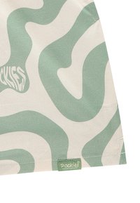 Grønn og kremmønstret stoff med bølgete design; har et merke merket "Pockies® Couch Couture" nederst på kanten. Glatt tekstur.