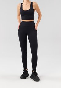 Svart sport-bh med breda axelband och ribbad textur, kombinerad med svarta högmidjade tights med sidofickor och en slät yta.