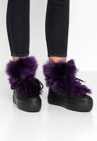Fialové kožené ankle boty z umělé kožešiny s černými robustními podrážkami a tkaničkami, s chlupatým lemem a hladkým koženým vzhledem.