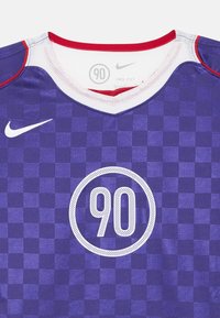 Purpura rūtiņu Nike krekliņš ar sarkanu apkakli, ar apaļu baltu grafiku centrā, kurā ir redzami "90". Izgatavots no elpojoša Dri-FIT materiāla.