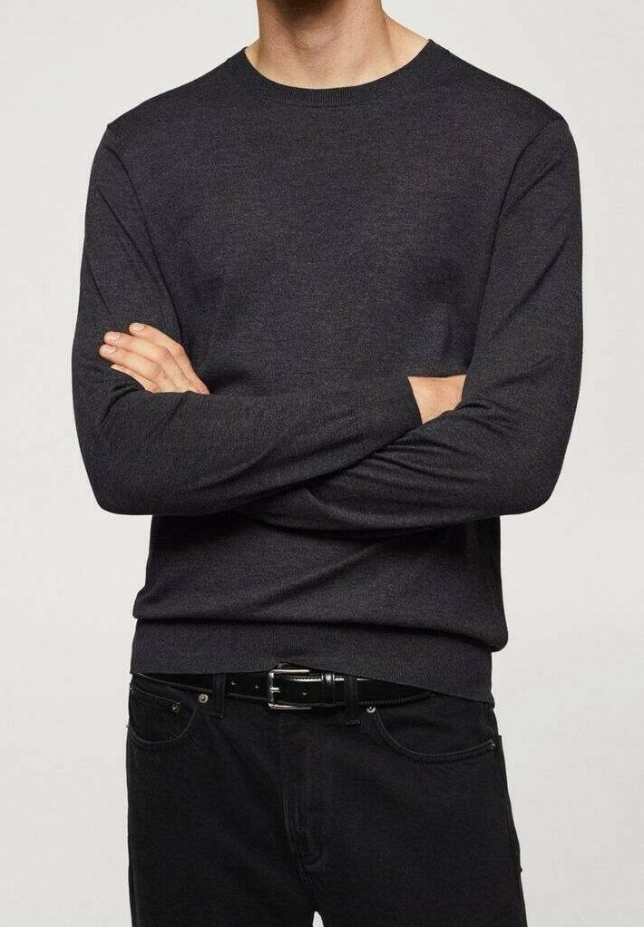 Homme portant un pull à col rond gris foncé à manches longues et un pantalon noir avec une ceinture noire, debout les bras croisés.