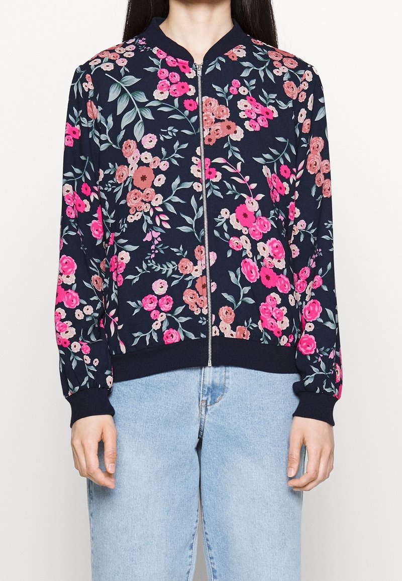 Blommig bomberjacka i marinblått med rosa och orange blommor, långa ärmar, ribbade ärmslut och dragkedja framtill. Textilen har en smidig yta.