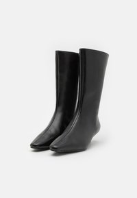 Bottes en cuir noir avec une tige haute, bout pointu et design sans couture. Texture lisse avec une fermeture éclair centrale pour un enfilage facile.