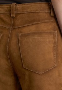 Bruine suede broek met een gladde textuur, achterzak en contrasterende stiksels. Getailleerde pasvorm met een klassieke tailleband.