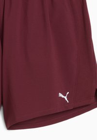 Burgundy sportlikud lühikesed püksid külgslitiga ja valge Puma logo vasakul all. Keskendutakse mugavusele ja sooritusele spordiüritustel.