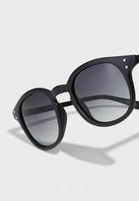 Schwarze Sonnenbrille mit großen, runden Fassungen und grauen Verlaufsgläsern. Mit kleinen silbernen Akzenten an der Fassung. UV400-Schutz.