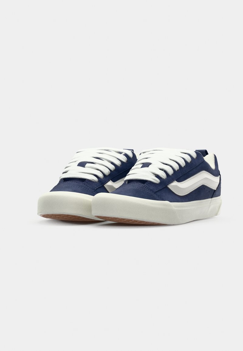Marineblaue Sneakers mit weißen Schnürsenkeln, weißem Seitenstreifen, strukturiertem Wildleder- und Gummi-Obermaterial sowie einer hellen Gummisohle.