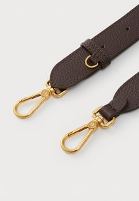 Correia de pele castanha com acabamento texturizado, apresentando clips e ferragens em metal dourado. Inclui um anexo em forma de laço e fivela ajustável.