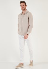 Heller beiger Langarmhemd mit einer Brusttasche, weiße Hose und hellbraune Sneakers. Glattes Material und Knopfverschlussdetails.