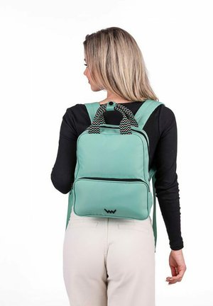 Mátově zelený batoh s černobílými zigzagovými akcenty, dvěma horními držadly a přední kapsou na zip. Kompaktní obdélníkový design.
