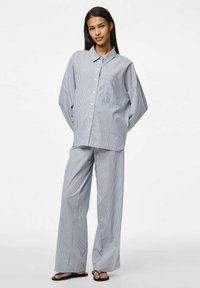Službena kombinacija svijetloplave i bijele prugaste košulje i širokih hlača, s džepom na košulji. Glatka tkanina s opuštenim dizajnom.