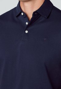 Polo bleu marine en coton, avec col, trois boutons et un petit logo brodé noir sur la poitrine.