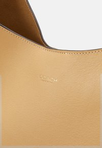 Gros plan sur un sac à main Coach en cuir fauve montrant la texture lisse, les coutures soignées et le logo doré embossé "Coach New York".