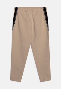 Beiga tapered byxor med svarta sidpaneler och vit piping, elastisk midja och sidofickor, uppvisade platt på en vit bakgrund.