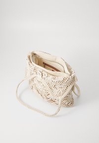 Open weave, cream-colored handbag with a textured design, adjustable braided strap, and an inner zippered pocket. Features a button closure.