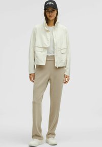 Lätt off-white jacka med ficklock, parat med beige byxor. Vita sneakers och en svart keps fulländar looken.