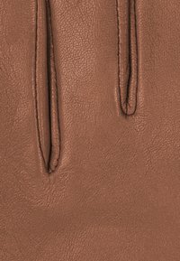 Braunes Leder mit texturierter Oberfläche, sichtbaren Nähten und langen Schnitten. Einfaches Design betont die natürliche Maserung.