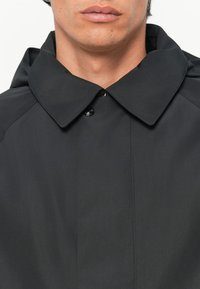 Must vest, mille laia kraega, ühe nupuga kinnitamine ja sile tekstuur; minimalistlik disain ilma nähtavate mustrite või aktsentideta.