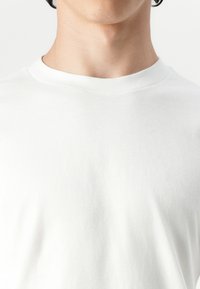 Tricou alb din bumbac cu guler rotund și mâneci scurte; textură netedă fără modele sau accente. Accentul este pe guler și zona pieptului.