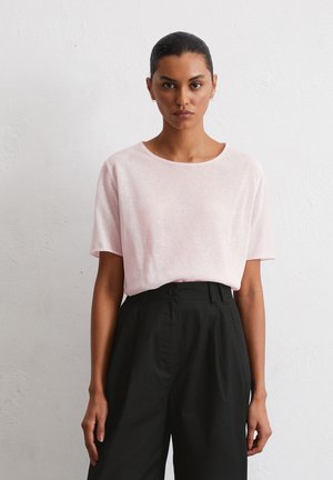 T-shirt rose clair à manches courtes dans une coupe décontractée, associé à un pantalon taille haute noir à jambes larges. Encolure ronde simple, texture douce.