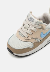 Beżowe i jasnoniebieskie buty sportowe z siateczki i skóry, z sznurowadłami, wyściółką na kołnierzu oraz teksturowaną czarną podeszwą.