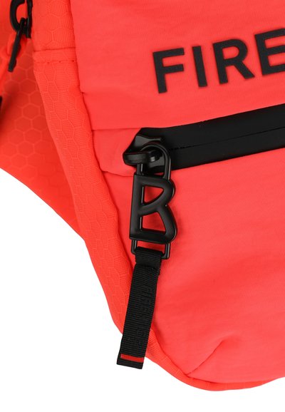 Světlý korálový batoh s texturovaným hexagonálním vzorem, černými zipovými akcenty a výrazným černým písmenem "B" na sponě.