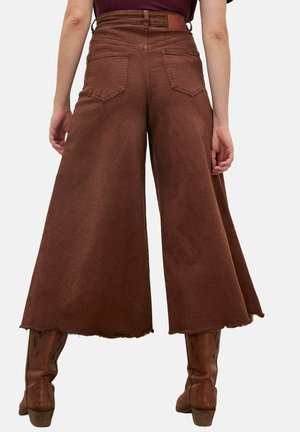 Bruine brede culottes van denim, met een rauwe zoom, twee achterzakken en een hoge tailleband. Gemaakt met bruine laarzen.